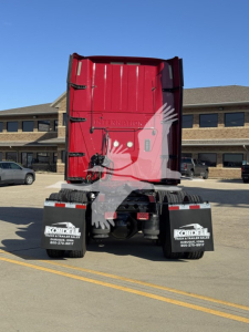 Truck rear view showing red sleeper cab with black mud flaps and bumper, dealership logos, and clear sky.