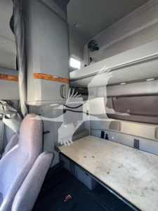 Cab interior of a sleeper truck showing bunk area with mattress surface, storage shelf, and window.