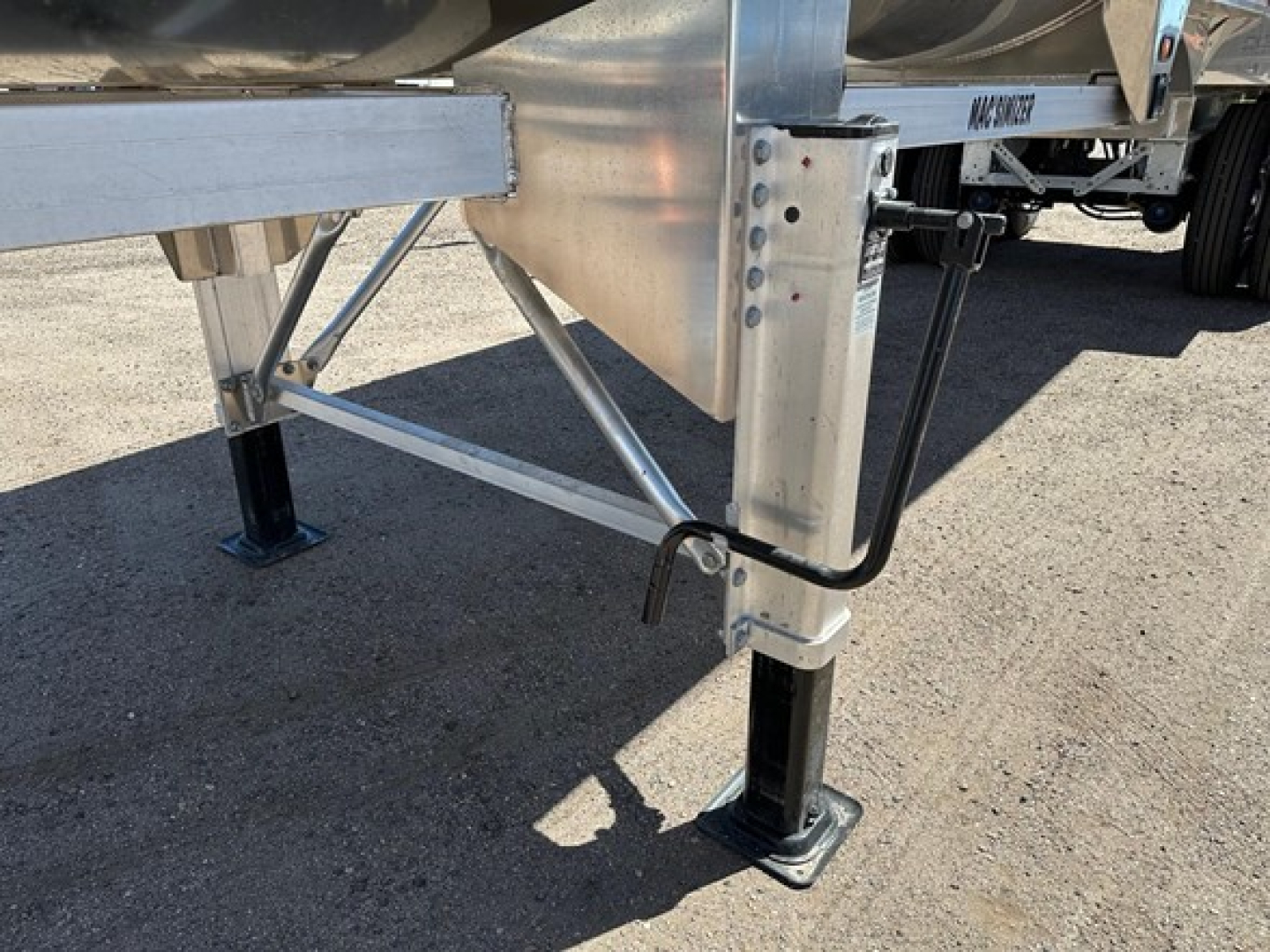 Trailer landing gear and undercarriage of a half-round aluminum end dump trailer showing stabilizing legs, frame braces, and jack footpads.