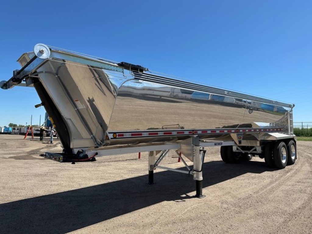 Semi-dome style end dump trailer in polished aluminum showing raised hinged tail and dual rear axles with landing gear, side reflective tape.