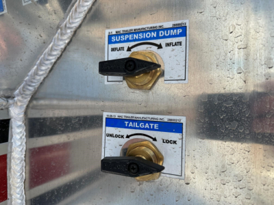 Trailer control panel with suspension dump and tailgate levers on a metal surface showing labels 'SUSPENSION DUMP' and 'TAILGATE' with handle positions.