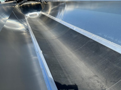 Aluminum end dump trailer interior showing smooth curved walls and joint seams along the inner surface.