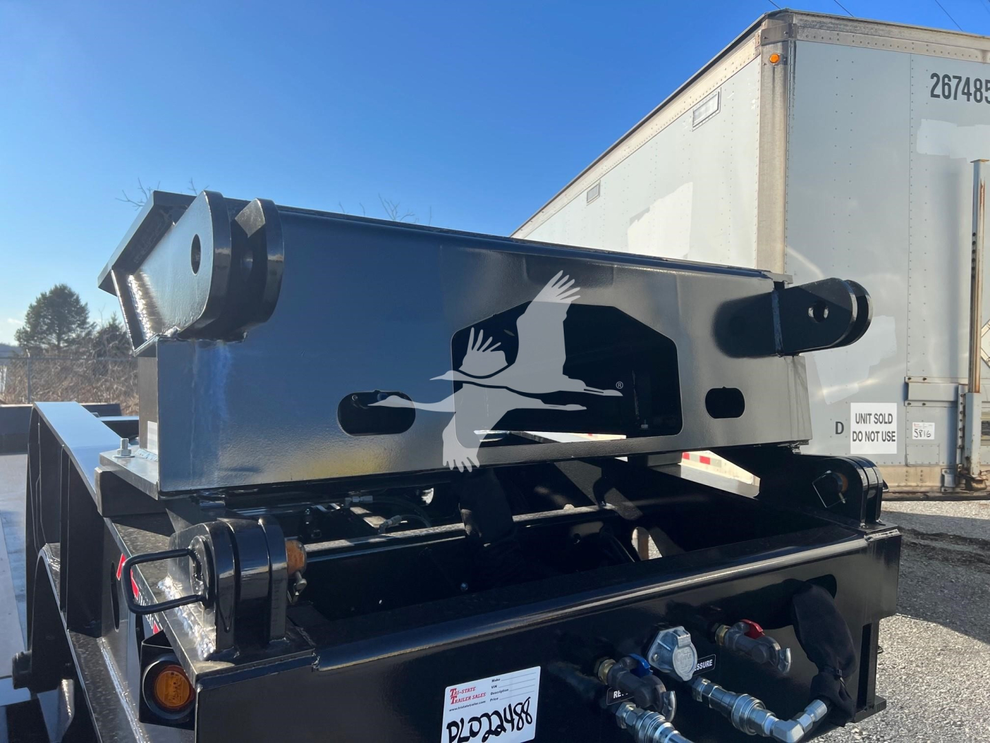 Trailer hitching/flip neck metal frame showing hydraulic equipment and mounting hardware on a black trailer under clear sky.
