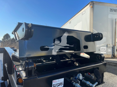 Trailer hitching/flip neck metal frame showing hydraulic equipment and mounting hardware on a black trailer under clear sky.