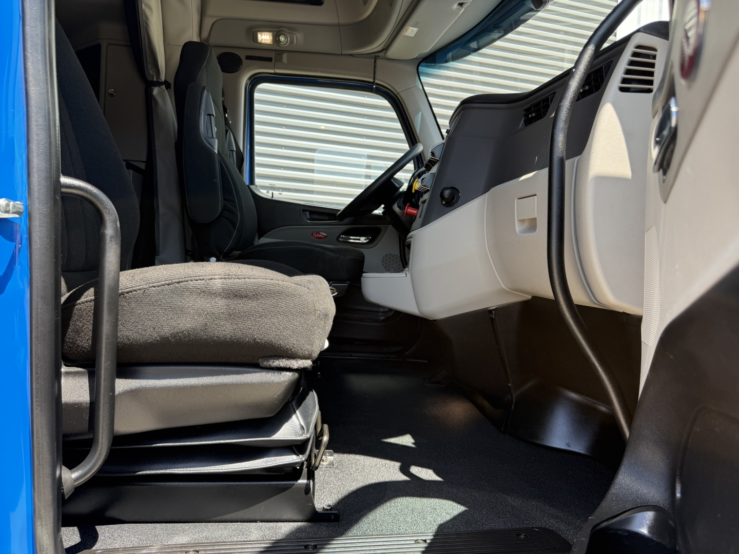 Truck cab interior of a 2022 Peterbilt 579, driver seat and dashboard visible from open door, light gray interior with black floor and steering wheel.