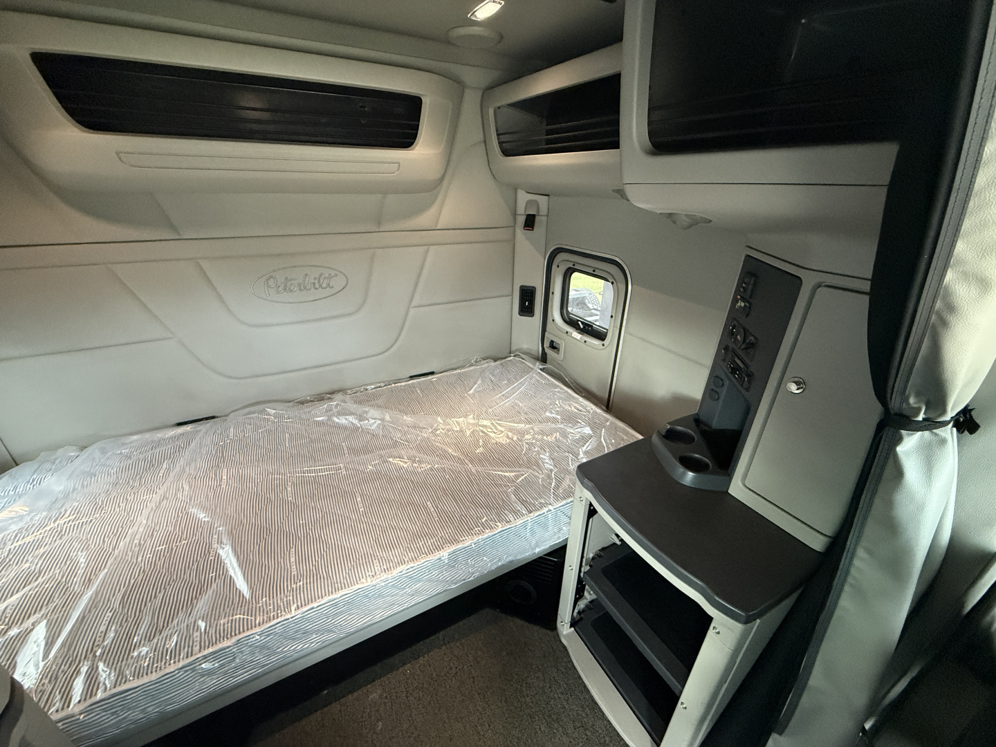 Peterbilt 579 cab sleeper interior showing cargo bed with plastic cover and overhead storage/console area.