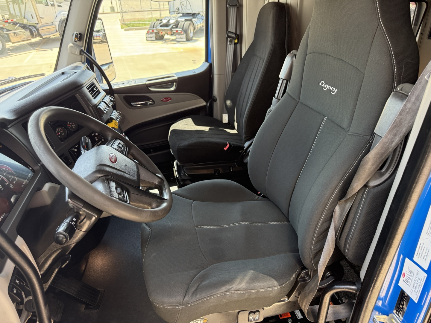 Peterbilt 579 truck cockpit with driver and passenger seats, interior view showing steering wheel, dashboard, and B58 seat covers, no visible text on seats