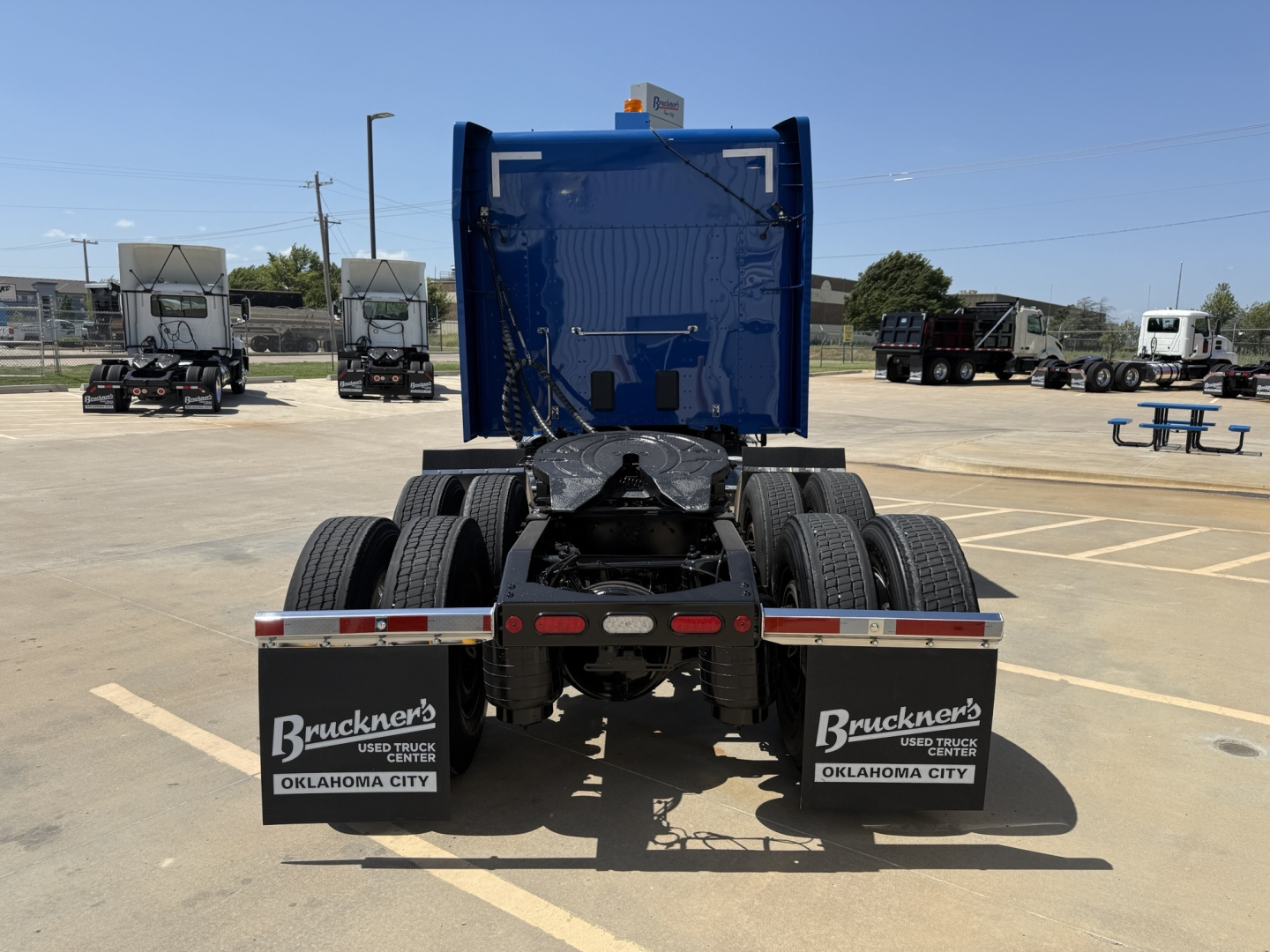 Rear view of a blue Peterbilt truck cab chassis showing dual rear wheels and mudflaps with Buckner's logo and Oklahoma City; stock plates and trailer hitch area visible.