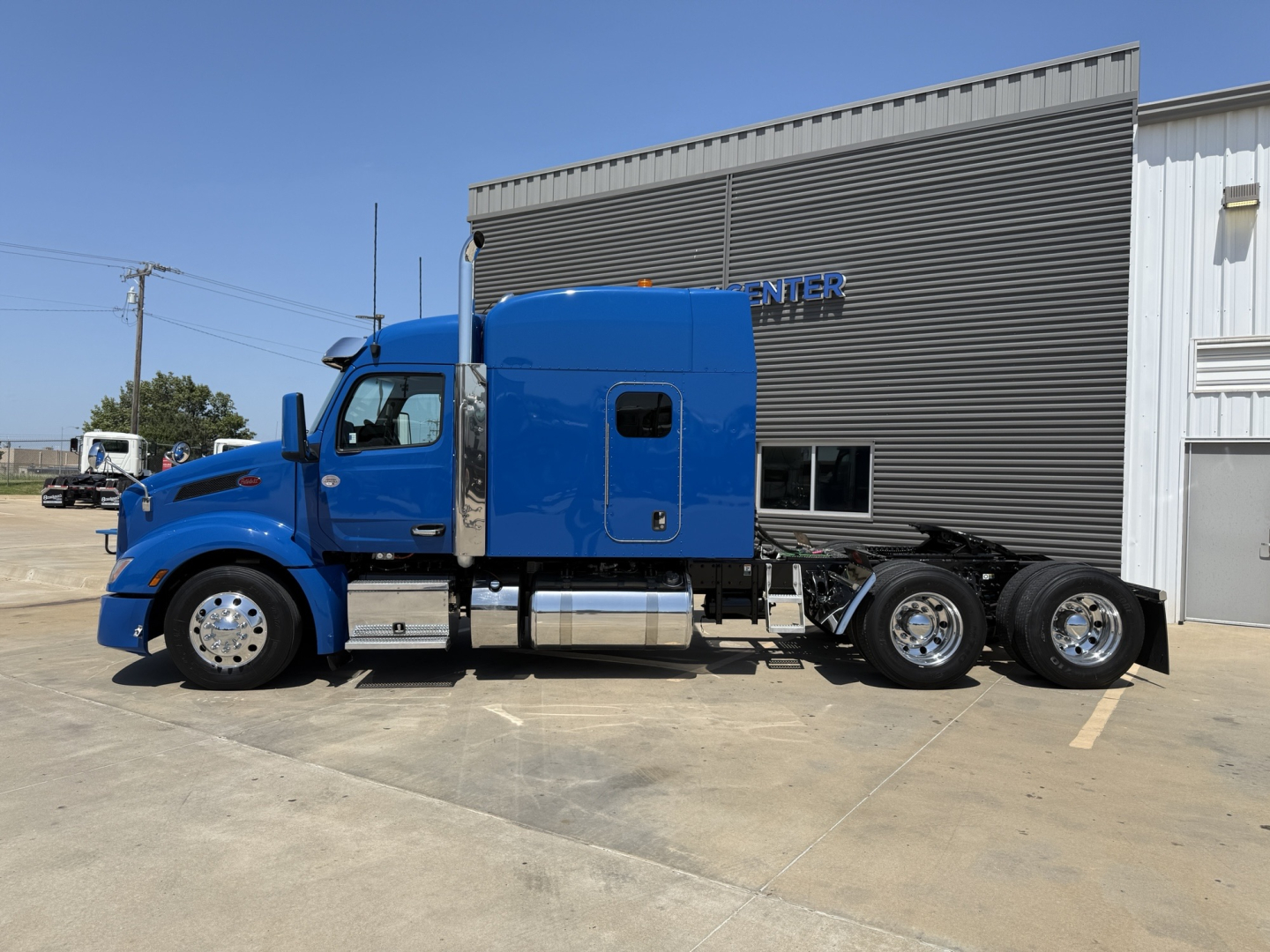 Peterbilt 579 tractor in blue, side view showing sleeper cab and dual rear axles, no visible damage.