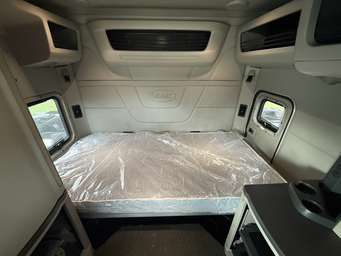 Peterbilt 579 sleeper cab interior cargo area with plastic-covered bunk bed and side windows.