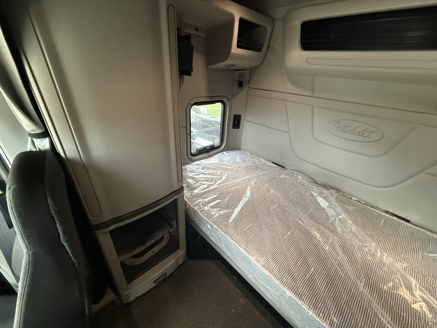 Peterbilt truck cab interior showing sleeper bed with plastic-covered mattress and Peterbilt logo on wall panel.