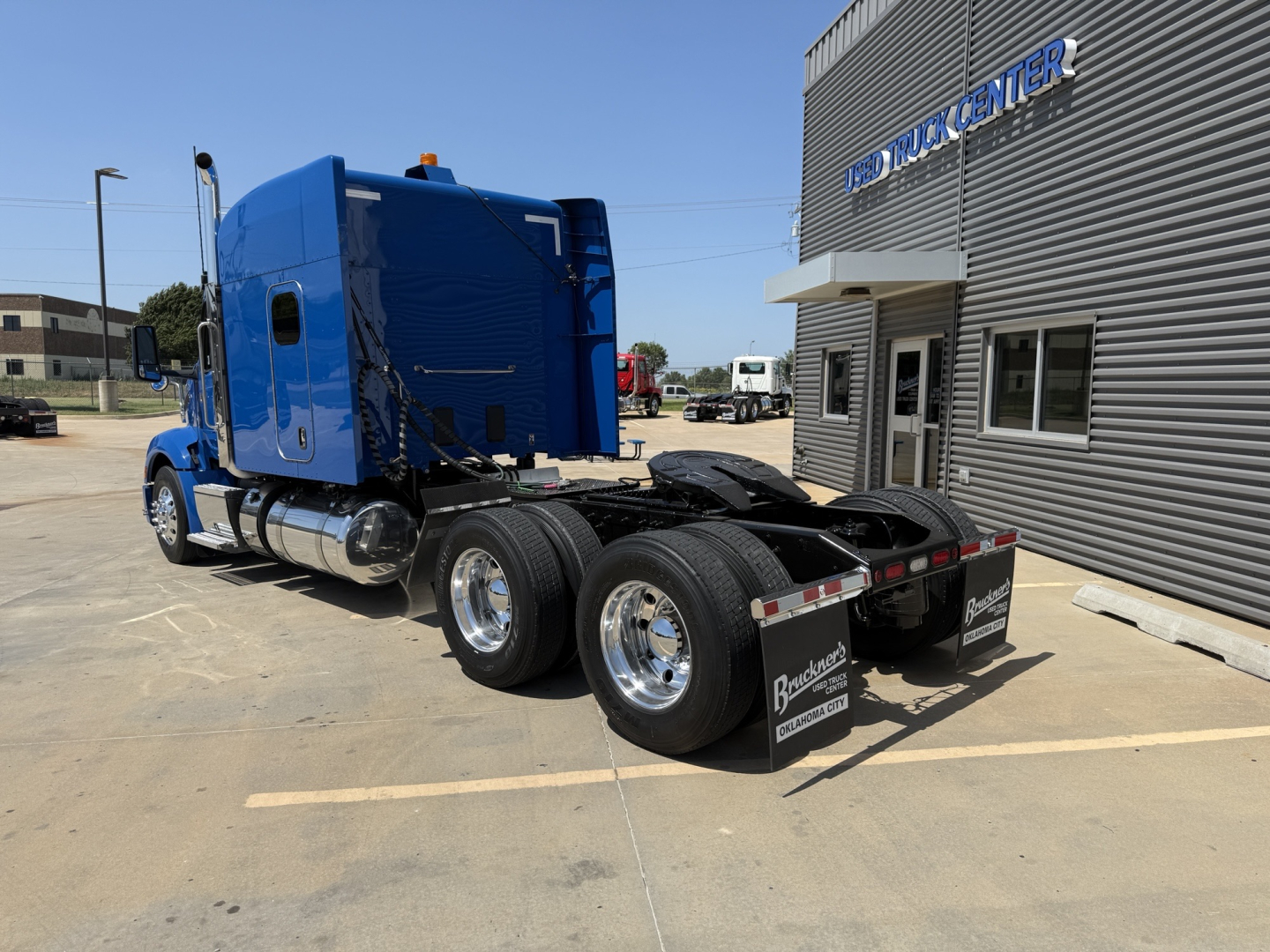 Peterbilt 579 tractor (blue) rear view showing chassis and dual rear axles with mudflaps; building with 'TRUCK CENTER' sign in background.