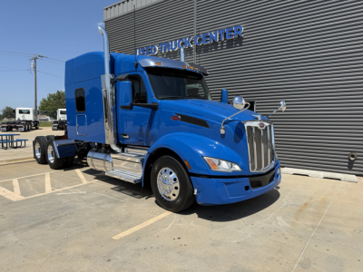 Peterbilt 579 tractor in blue, side view, front grille, chrome accents, sleeper cab, parked outside dealership.