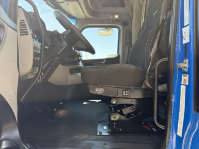 Peterbilt 579 cab interior showing driver seat and dashboard with steering wheel and floor pedals; base of seat with mounting hardware visible.