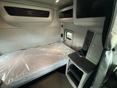 Peterbilt 579 cab sleeper interior showing cargo bed with plastic cover and overhead storage/console area.