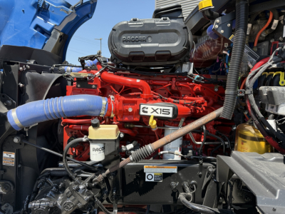 Peterbilt 579 engine bay showing red engine with PACCAR badge, blue coolant hose, and various components.
