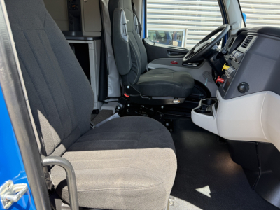 Peterbilt 579 cab interior showing driver seat and passenger bench, steering wheel, dashboard, and grey fabric seats