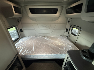 Peterbilt 579 sleeper cab interior cargo area with plastic-covered bunk bed and side windows.