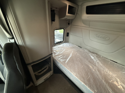 Peterbilt truck cab interior showing sleeper bed with plastic-covered mattress and Peterbilt logo on wall panel.