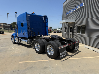 Peterbilt 579 tractor (blue) rear view showing chassis and dual rear axles with mudflaps; building with 'TRUCK CENTER' sign in background.