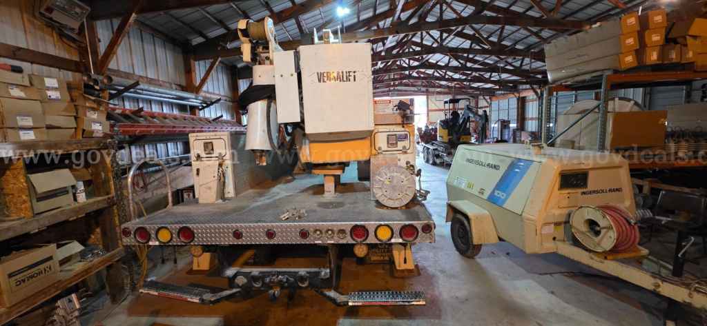 Truck yard scene with a boom truck on a trailer and a modular hydraulic unit labeled VEGMAJ? showing a crane rig, inside a warehouse.