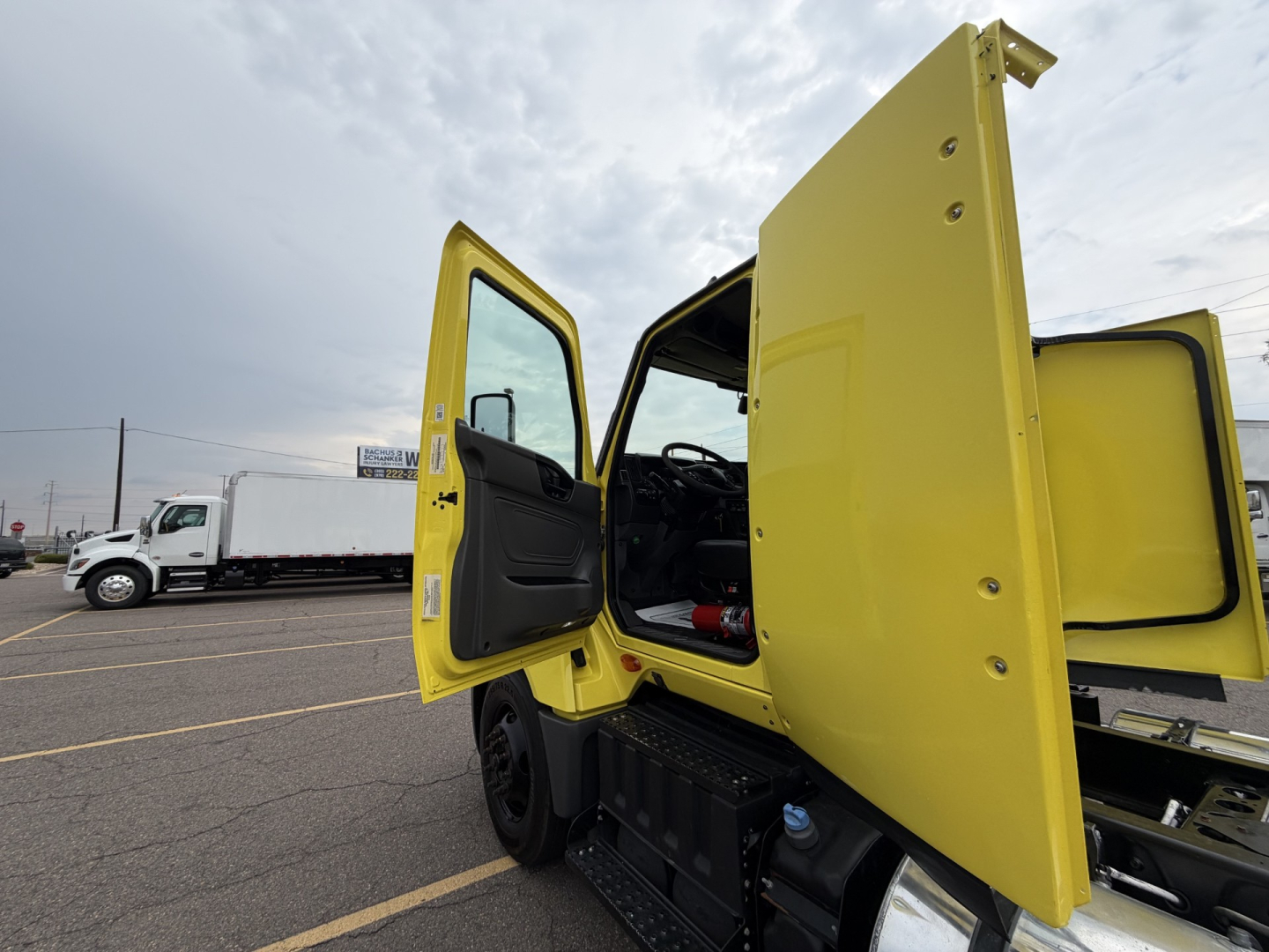 Truck cab with yellow doors open showing interior cab area and passenger side; side view in a lot with other trucks in background.