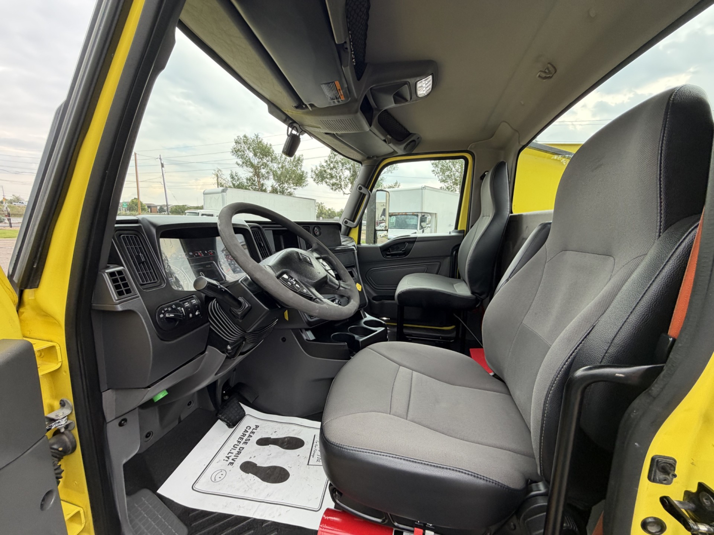 Truck cab interior of a 2023 International LT625 with gray seats, steering wheel, and dashboard visible from the driver’s side open door.