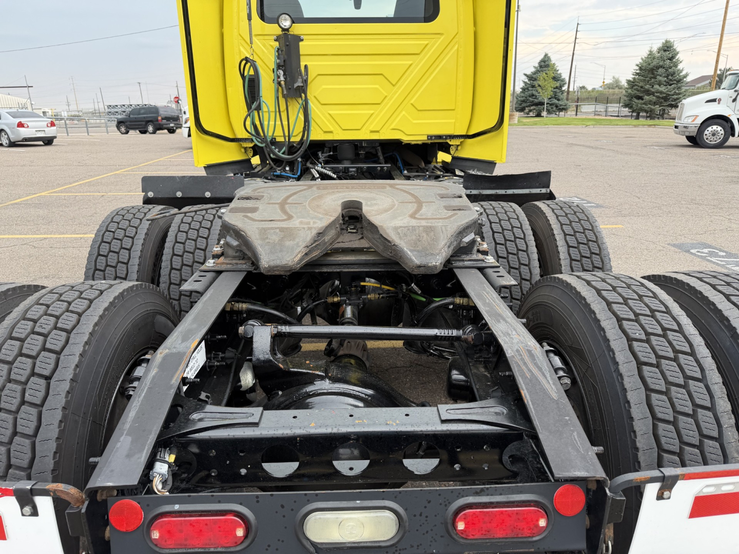 Truck chassis and rear view showing drivetrain and suspension components with MT tires; yellow cab in background; heavy-duty truck frame with drive axles.