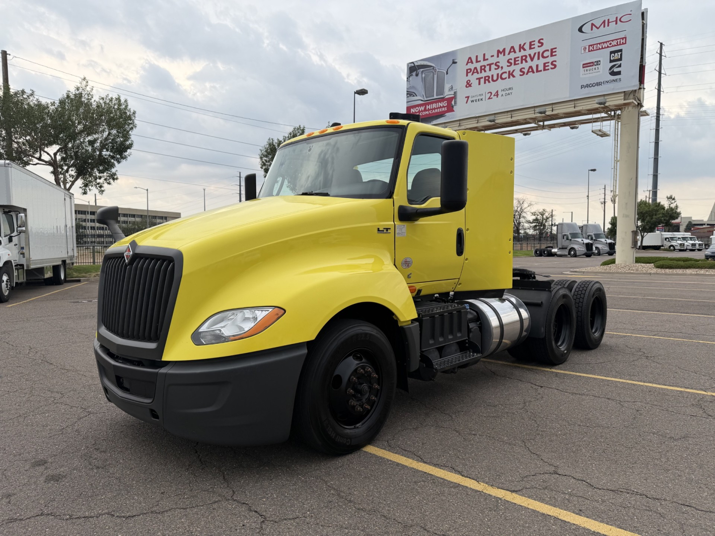 Yellow 2023 International LT625 daycab tractor truck in a parking lot, front-left view showing LT625 badge, large black grille, dual rear axles, and black front bumper.