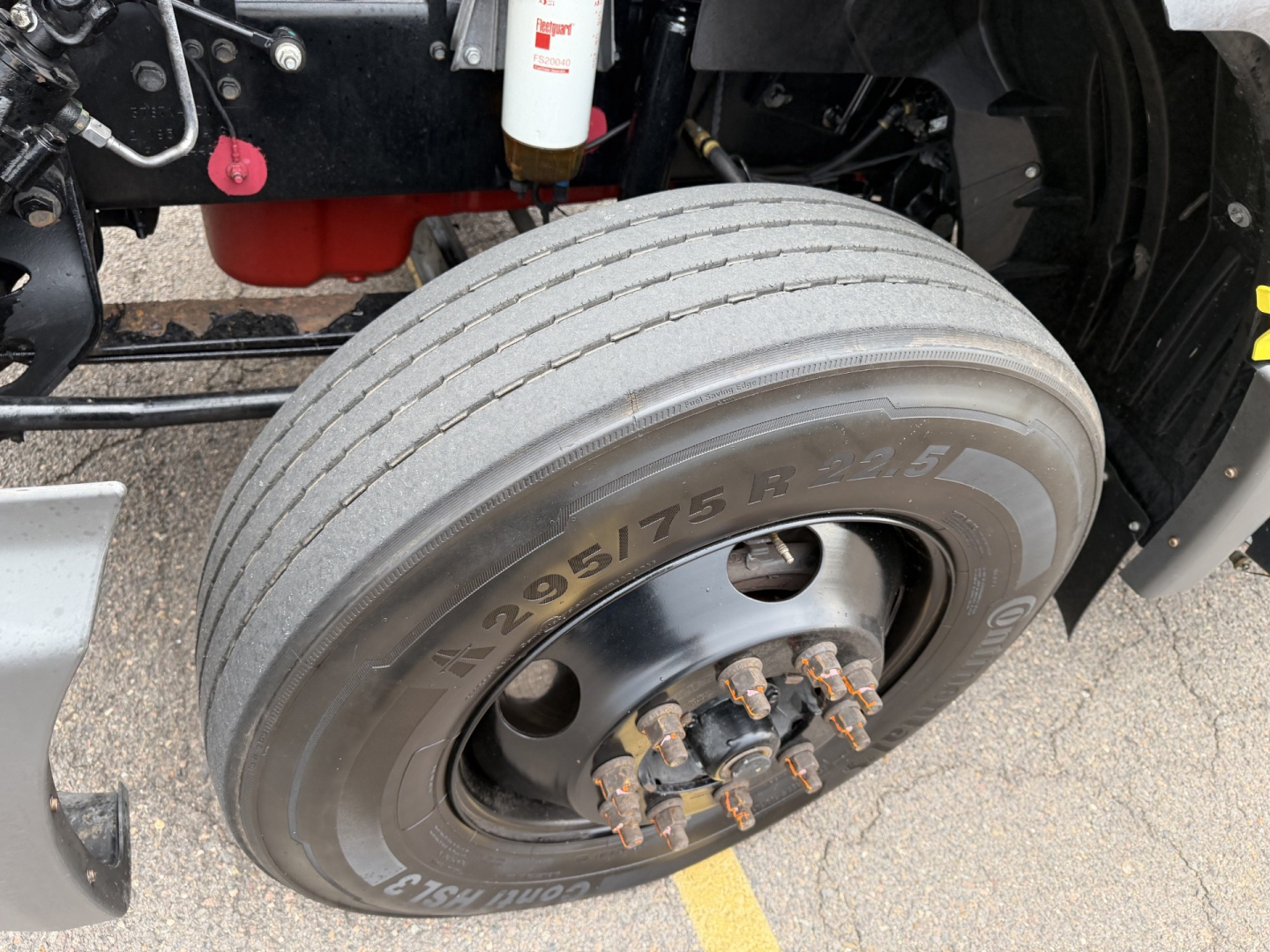 Truck front wheel showing 295/75R22.5 tire with lug nuts and part of suspension; visible label reads 295/75R22.5 on tire sidewall.
