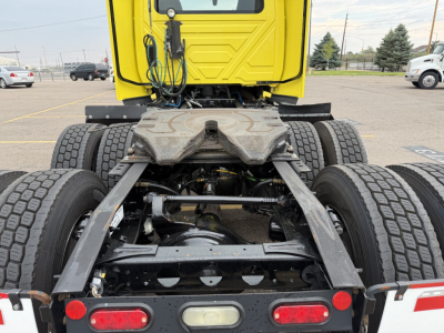 Truck chassis and rear view showing drivetrain and suspension components with MT tires; yellow cab in background; heavy-duty truck frame with drive axles.