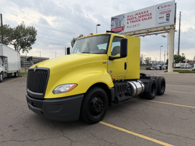 Yellow 2023 International LT625 daycab tractor truck in a parking lot, front-left view showing LT625 badge, large black grille, dual rear axles, and black front bumper.