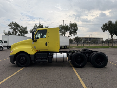 Truck side view showing yellow cab and chassis of a 2023 International LT625 with dual rear axles and fuel tank visible