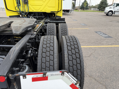 Semi tractor rear view showing tandem dual rear axles and part of a bright yellow sleeper cab; visible tires and frame; parking lot lines in background.