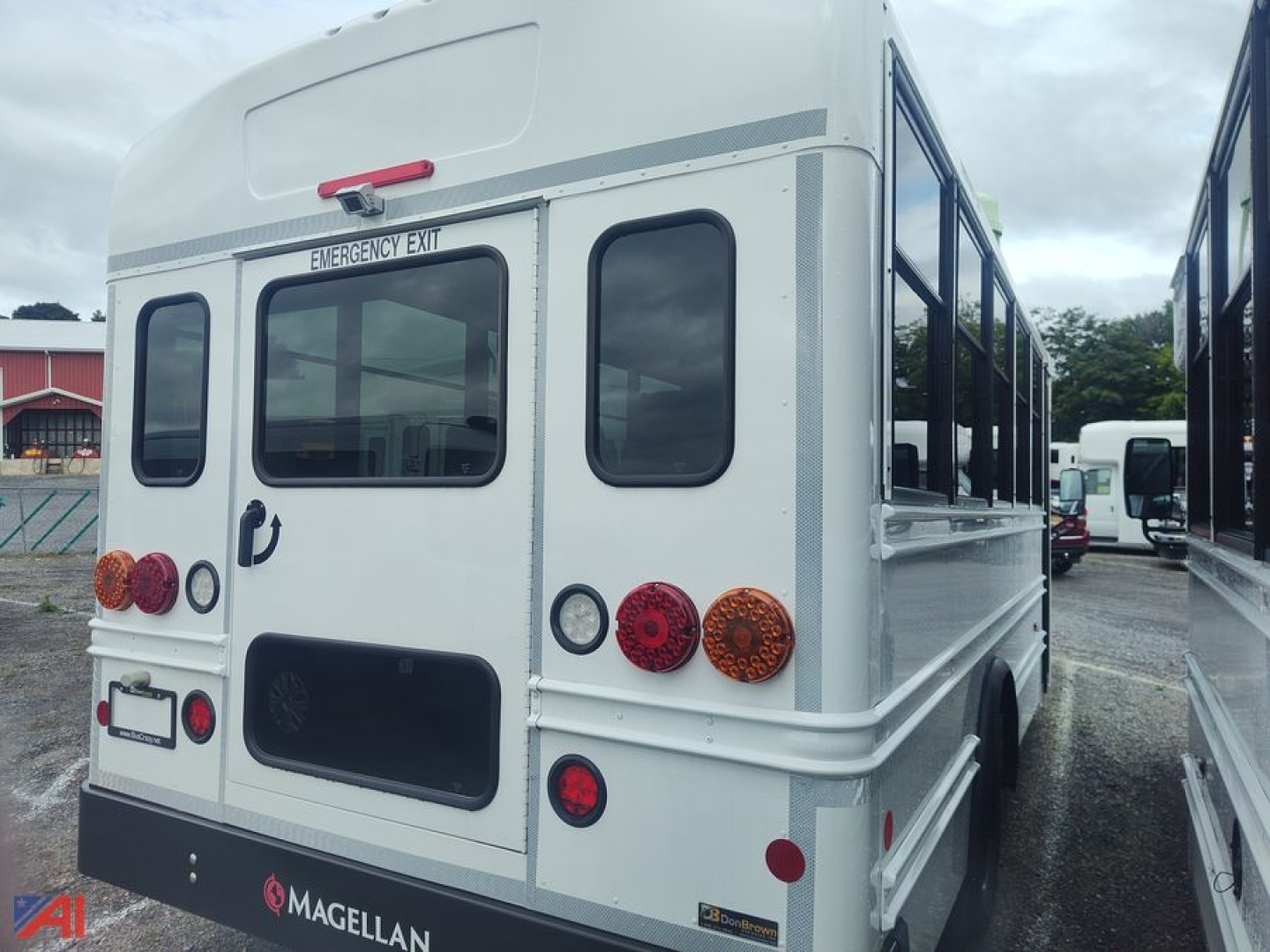 Bus rear view showing emergency exit window and Magellan brand badge, white body, red and amber lights, side trailer and bus exterior.