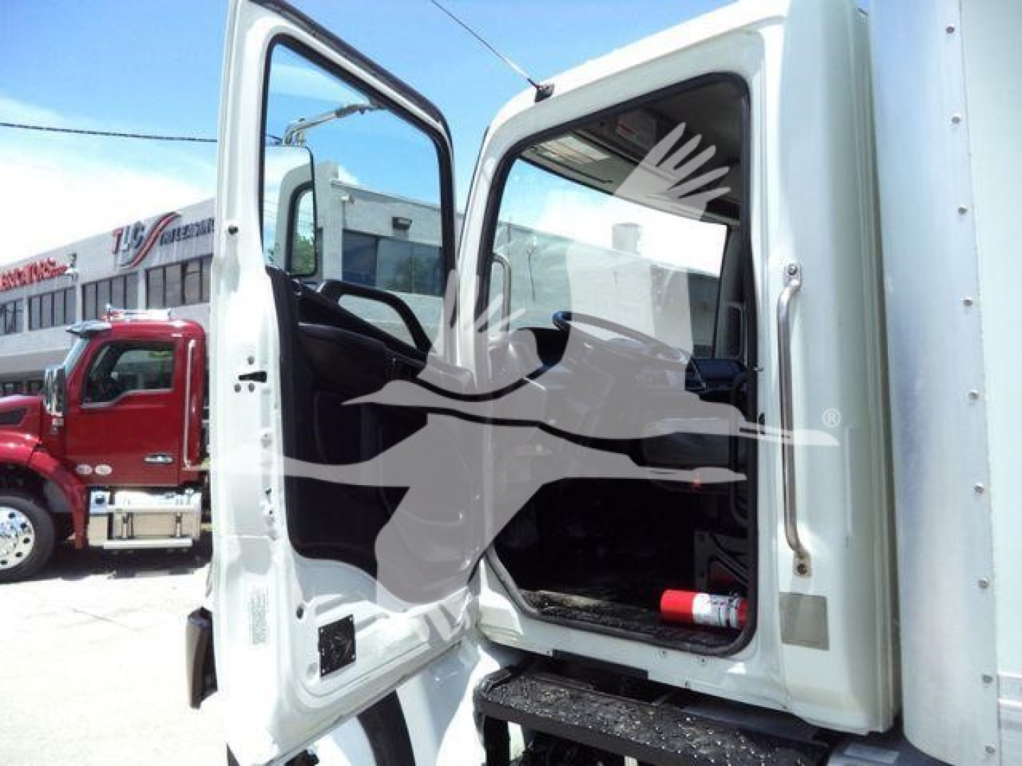 Image of a 2020 Hino 268A box truck with the driver’s door open. Interior cab visible; a fire extinguisher is in the cab area near the door. Other trucks and dealership building in the background.