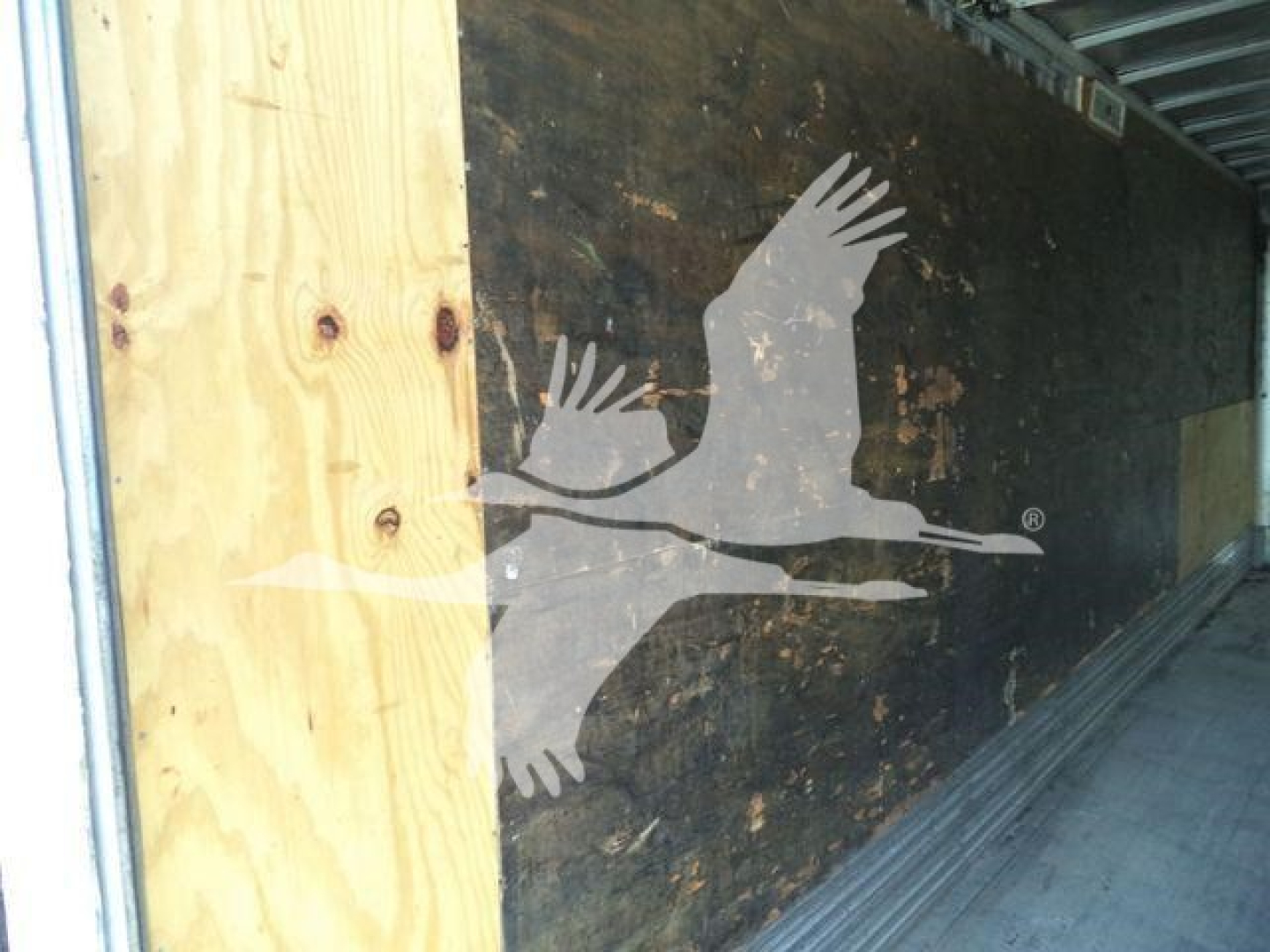 Truck cargo area interior with wooden panel and black wall, logo of two flying birds on side.