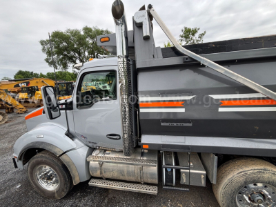 Truck side view showing International 7400 dump truck with gray cab and black dump body, chrome exhaust stack, side steps, and orange reflective stripe.