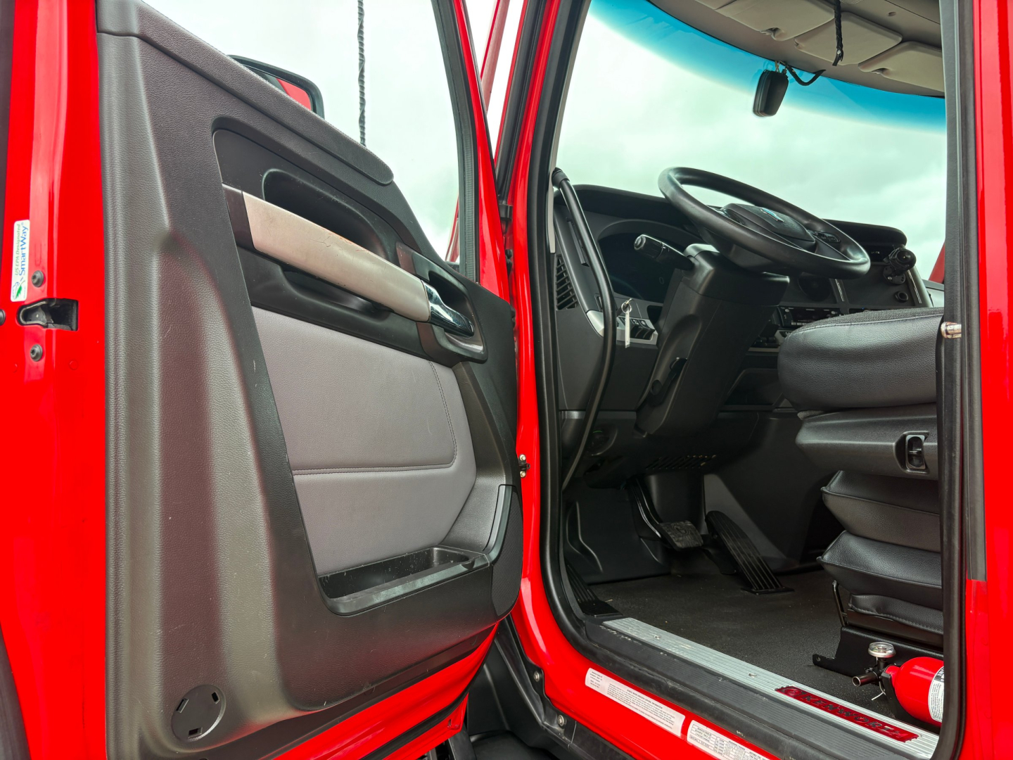 Kenworth T680 truck cab interior view from open driver door showing steering wheel and dashboard.