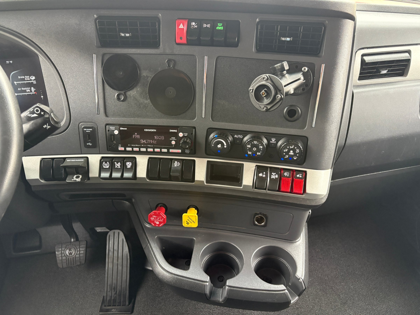Kenworth T680 dashboard and center console showing steering wheel, gauges, climate controls, ignition, and various switches in a sleeper cab.