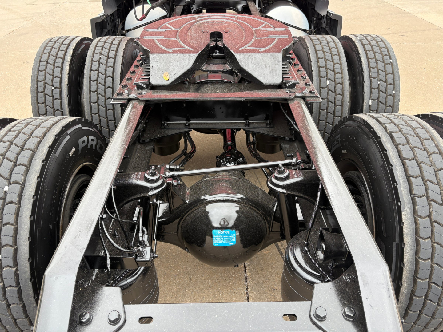 Kenworth T680 rear axle and suspension showing dual rear axles and drive components with spare blue label on differential.