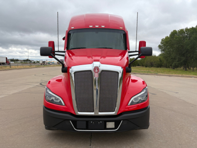 Kenworth T680 front view showing bold chrome grille, large headlights, red cab, black bumper, and side mirrors.