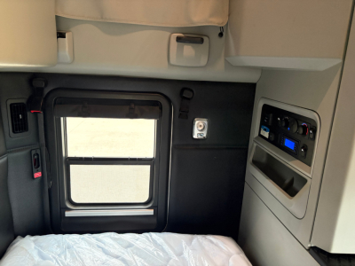 Kenworth T680 sleeper cab interior rear area showing window and control panel area on right with vent and storage; cab wall and door seam visible.