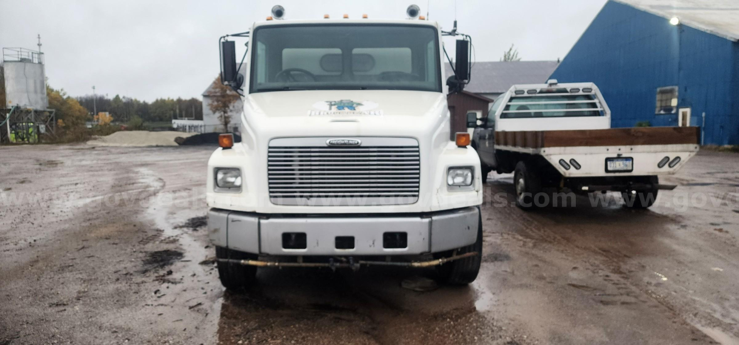 Front view of a white Freightliner FL70 sweeper truck showing grille, windshield, and headlights.