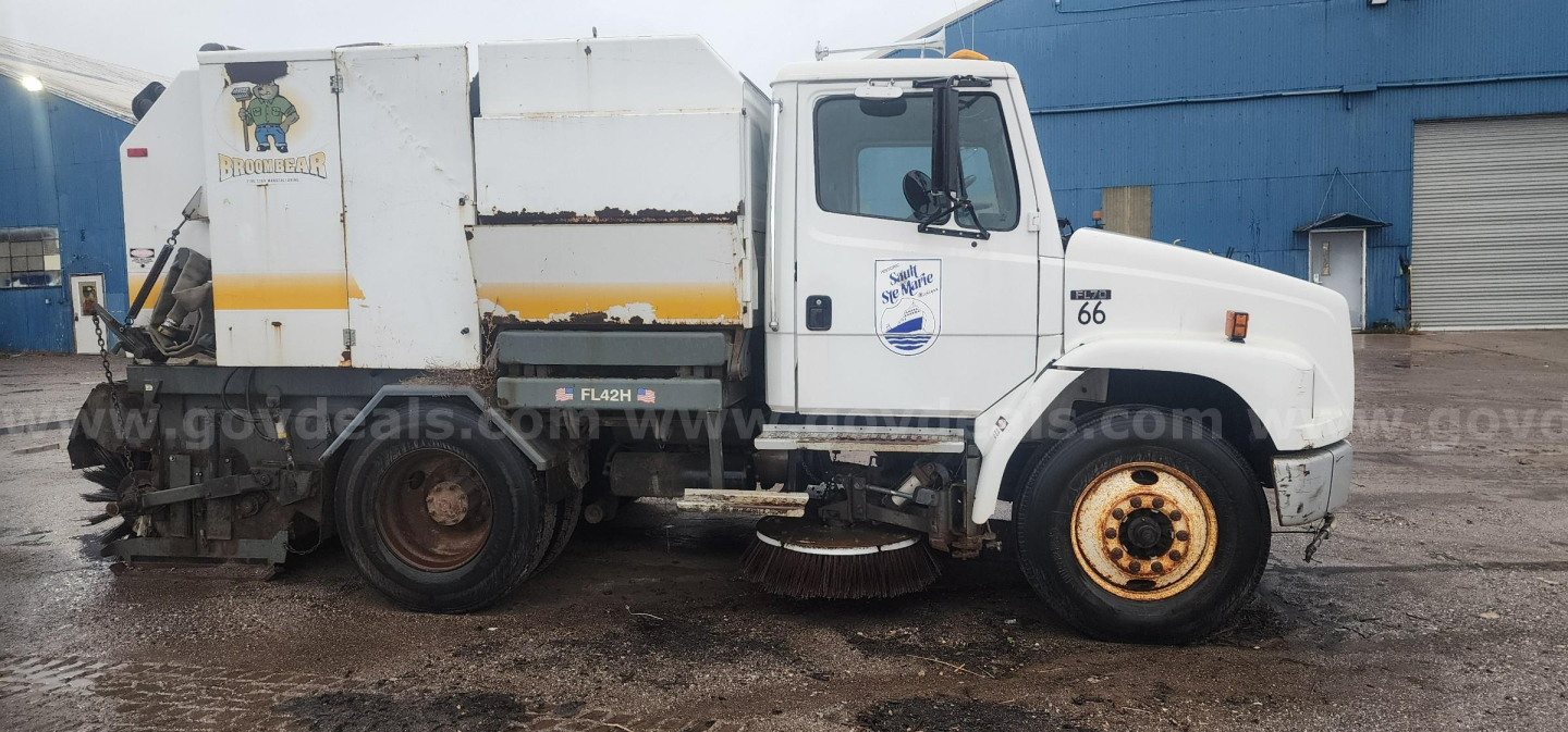 Freightliner FL70 street sweeper truck side view showing sweeping unit and debris hopper.