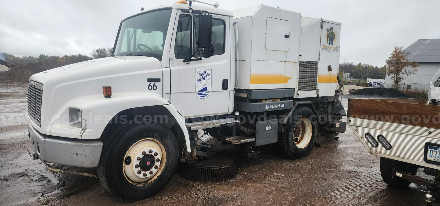 Sweeper truck: white 2000 Freightliner FL70 with side-mounted sweeping unit and cab doors; visible text includes fleet logo on door and number 66 on front fender.
