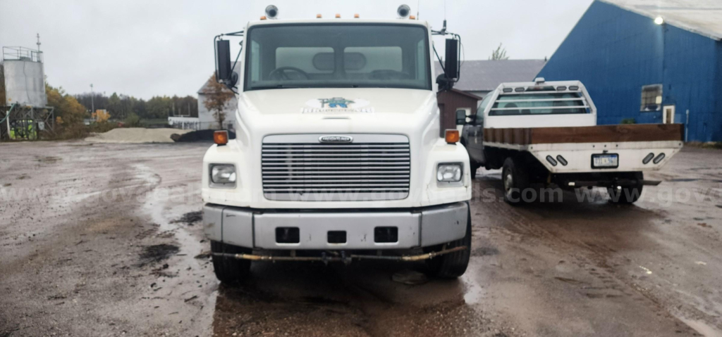 Front view of a white Freightliner FL70 sweeper truck showing grille, windshield, and headlights.