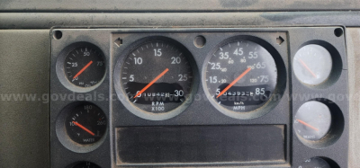 Dashboard gauges showing speedometer, tachometer, and fuel/engine indicators in a Freightliner FL70 cab; visible numbers include RPM x1000, MPH, and gauge needles.