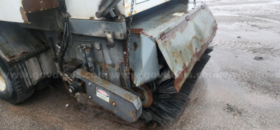 Sweeper attachment on a Freightliner FL70 showing brush assembly and side guards with rust and wear visible.
