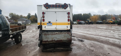 Rear view of a Freightliner sweeper truck with a yellow reflective stripe, tail lights, and a dirt-covered rear bumper; VIN plate not visible.